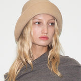 Person wearing a beige beanie and gray sweater against a white background