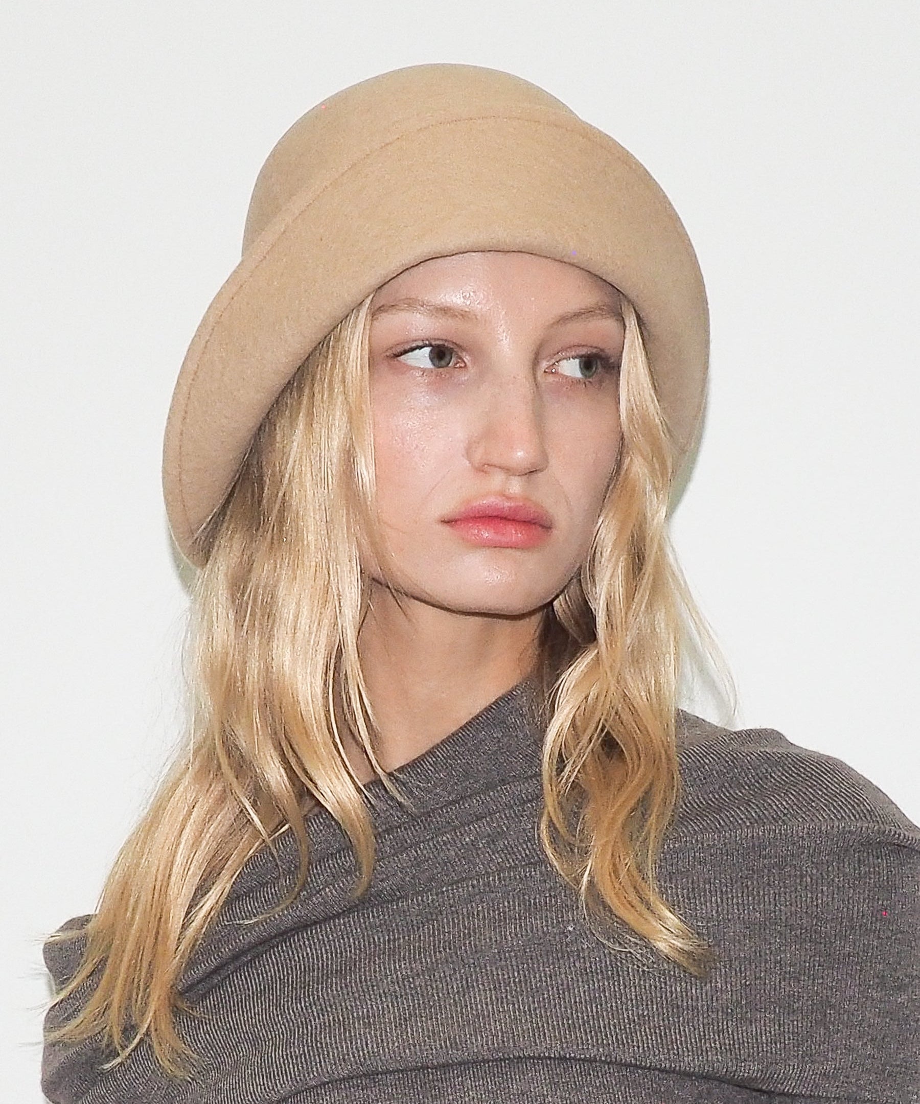 Person wearing a beige beanie and gray sweater against a white background