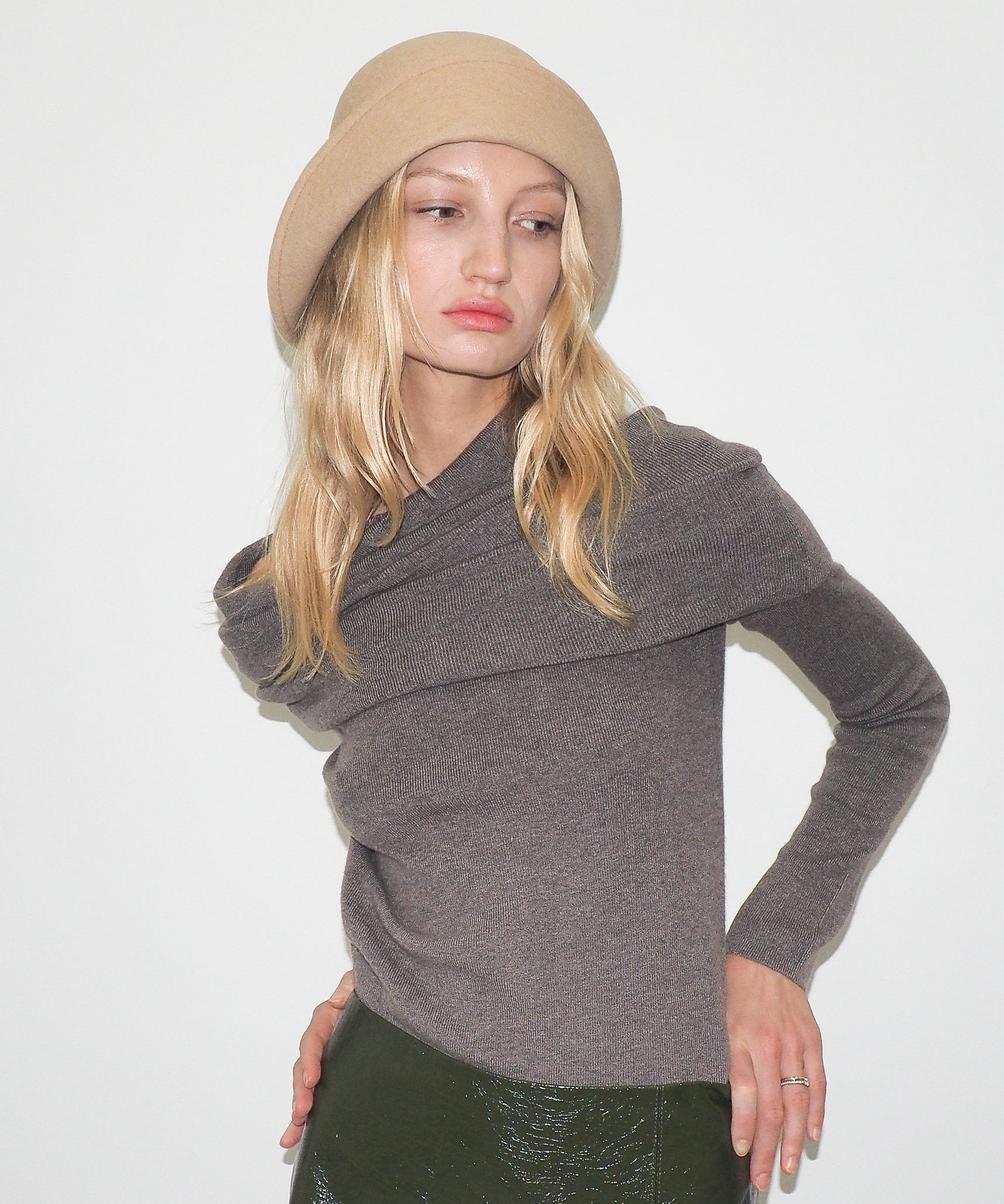 Woman wearing a gray sweater and beige beret against a white background