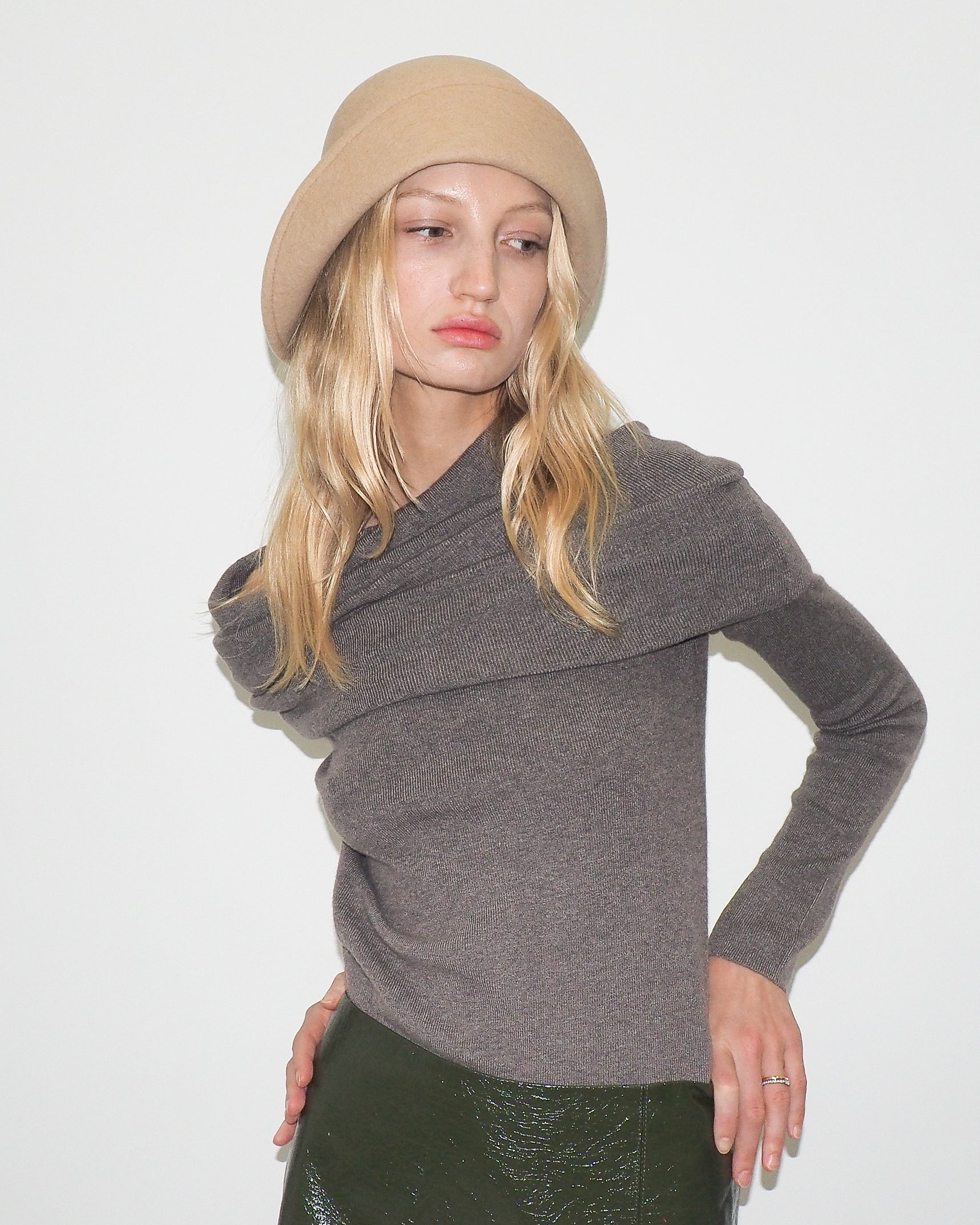 Woman wearing a gray sweater and beige beret against a white background