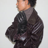 Person wearing a brown leather coat and black gloves against a white background