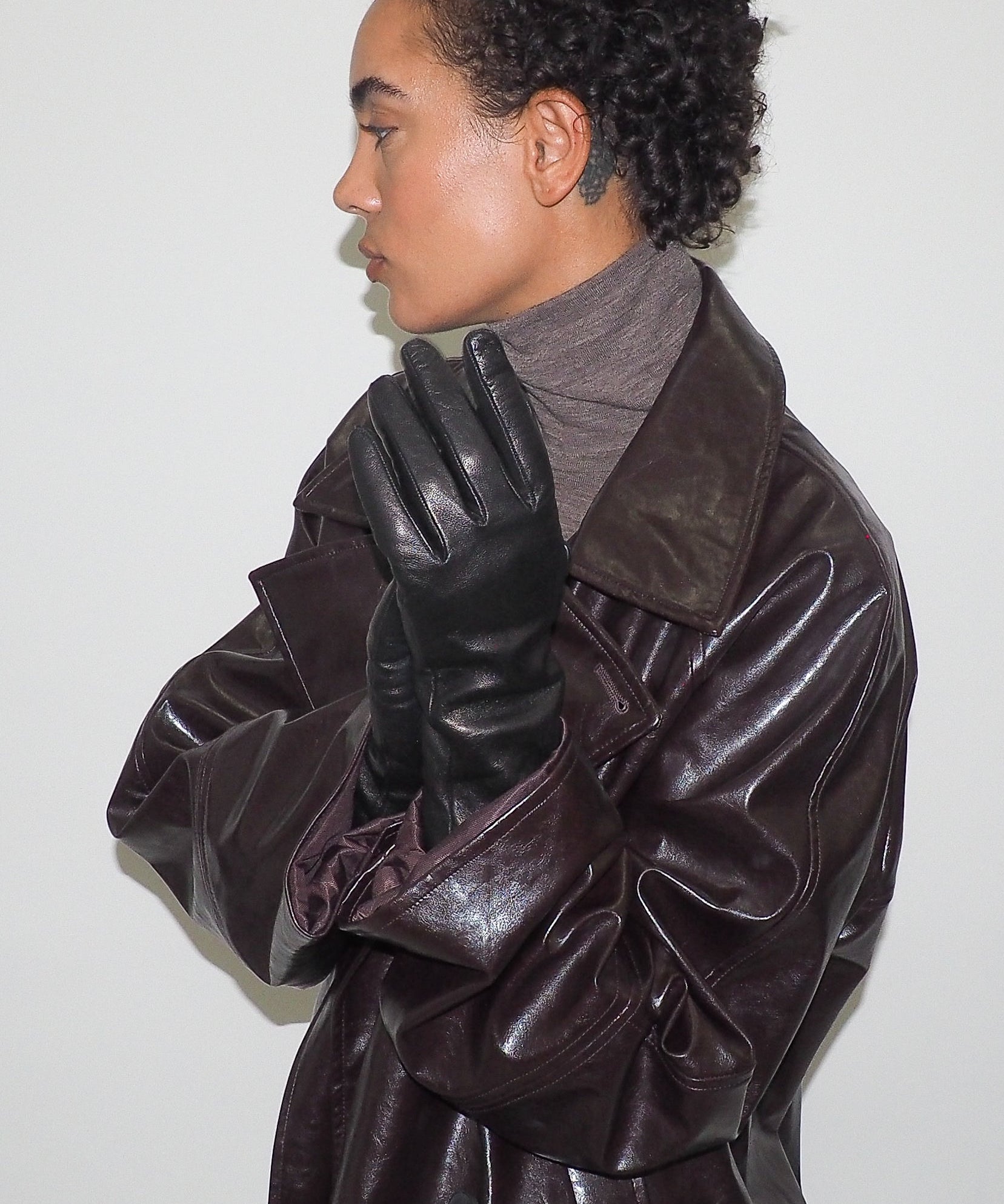 Person wearing a brown leather coat and black gloves against a white background