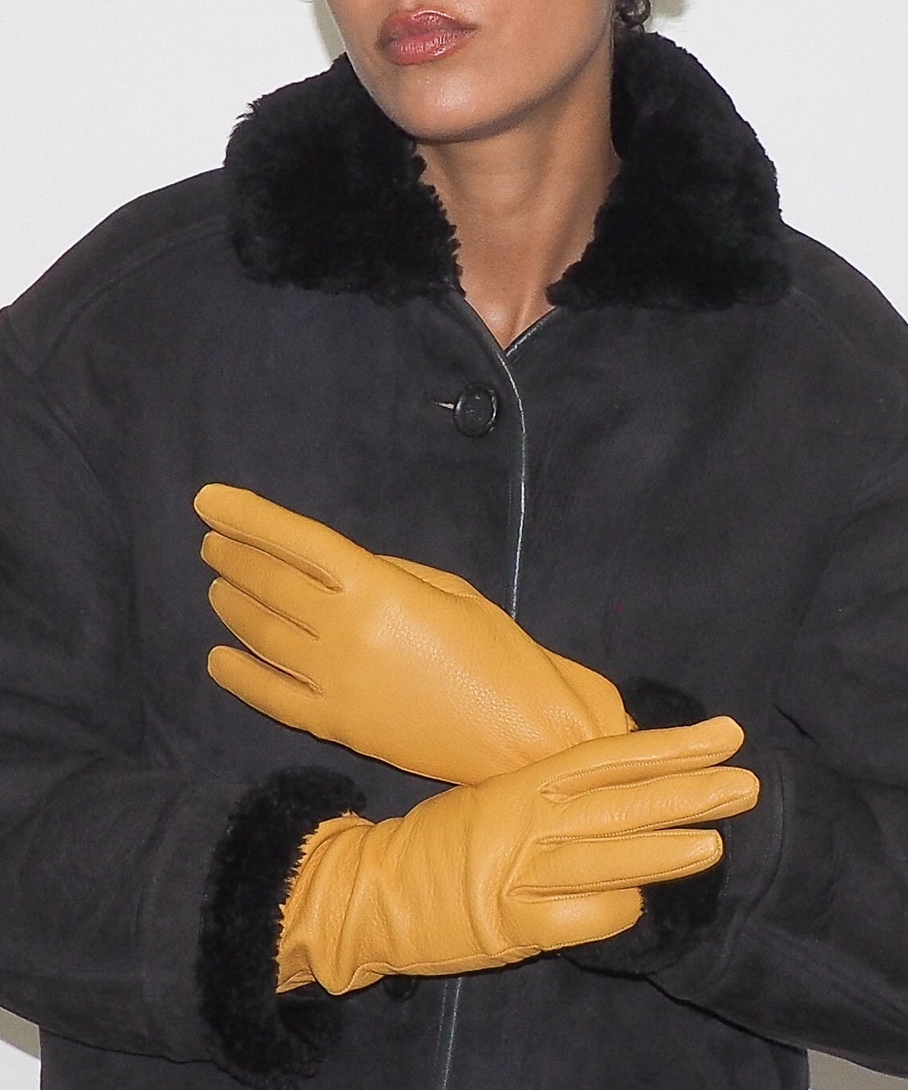 Woman wearing a black coat with fur collar and yellow gloves against a white background