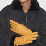 Woman wearing a black coat with fur collar and yellow gloves against a white background