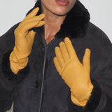 Person wearing a black coat with fur collar and yellow gloves against a white background