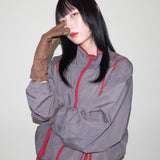 Person wearing a gray jacket with red accents against a plain background