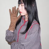Person wearing a gray outfit with red accents and brown gloves against a plain background