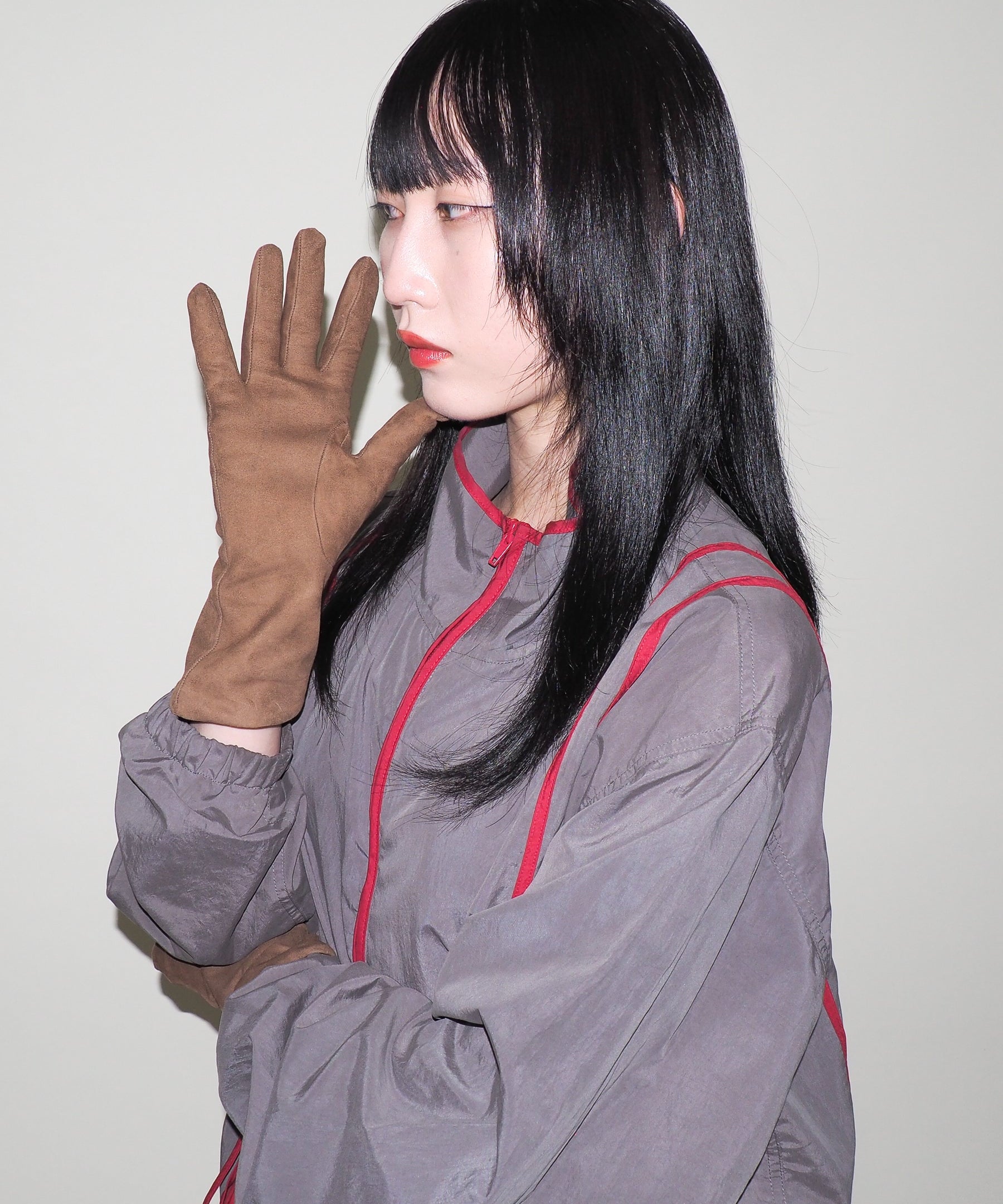 Person wearing a gray outfit with red accents and brown gloves against a plain background