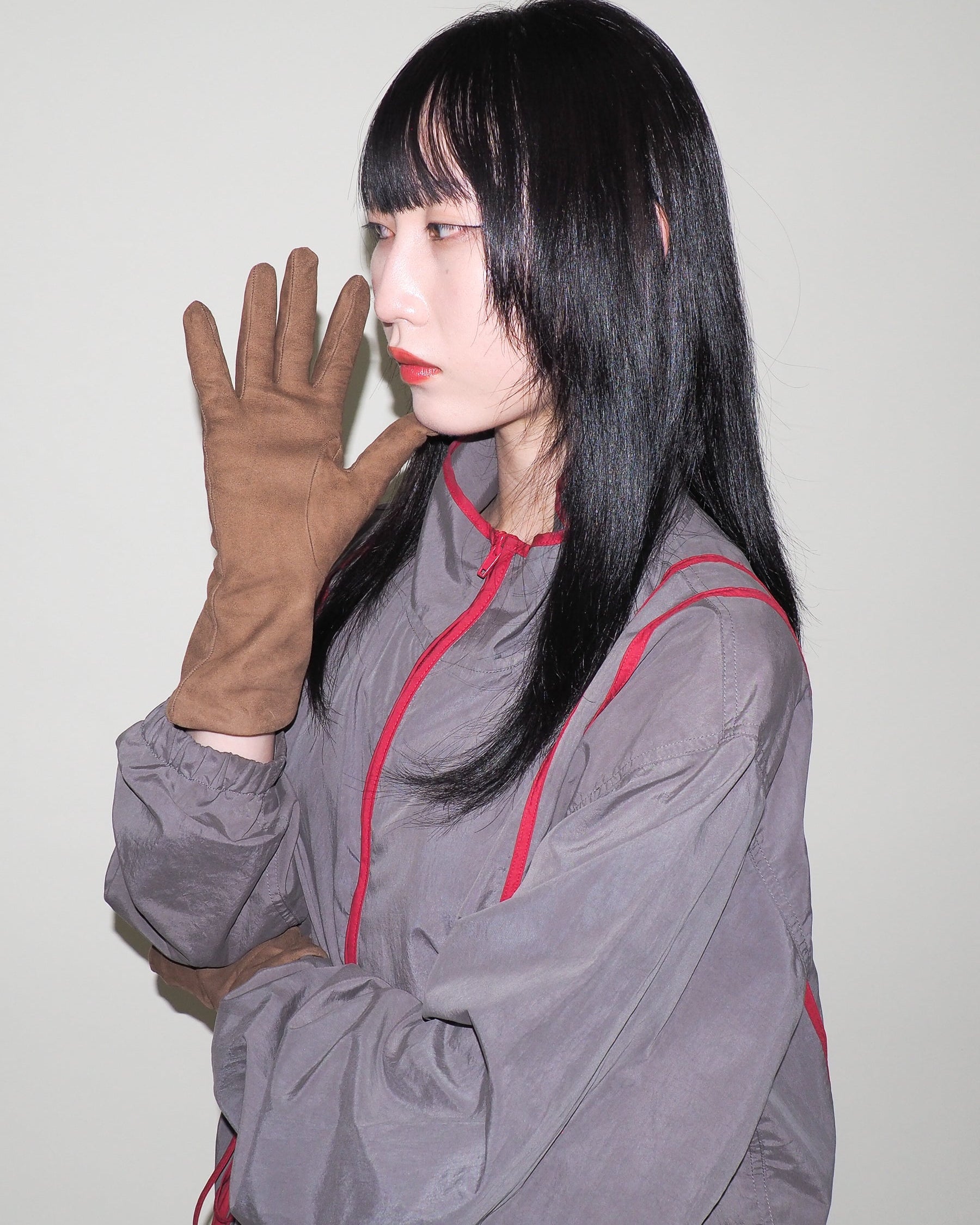 Person wearing a gray outfit with red accents and brown gloves against a plain background
