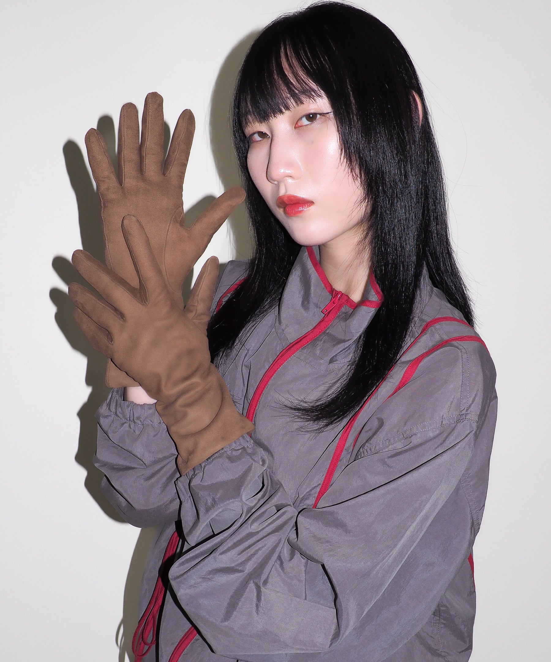 Person wearing a gray outfit with red accents and brown gloves against a white background