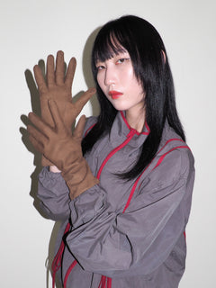 Person wearing a gray outfit with red accents and brown gloves against a white background