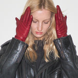 Woman wearing a black leather jacket and red gloves against a white background