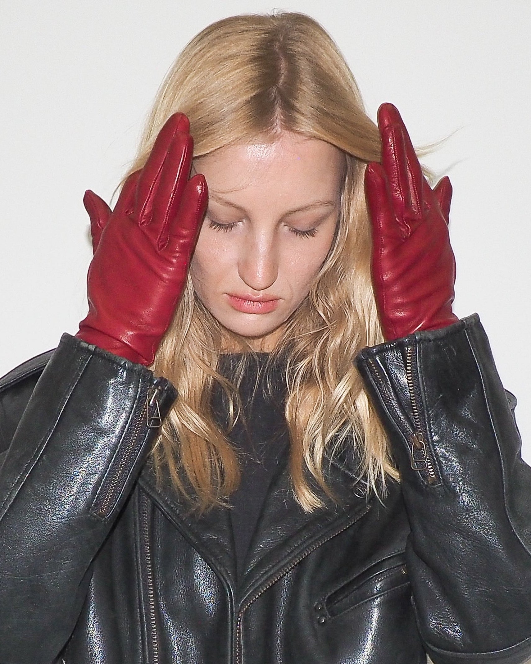 Woman wearing a black leather jacket and red gloves against a white background