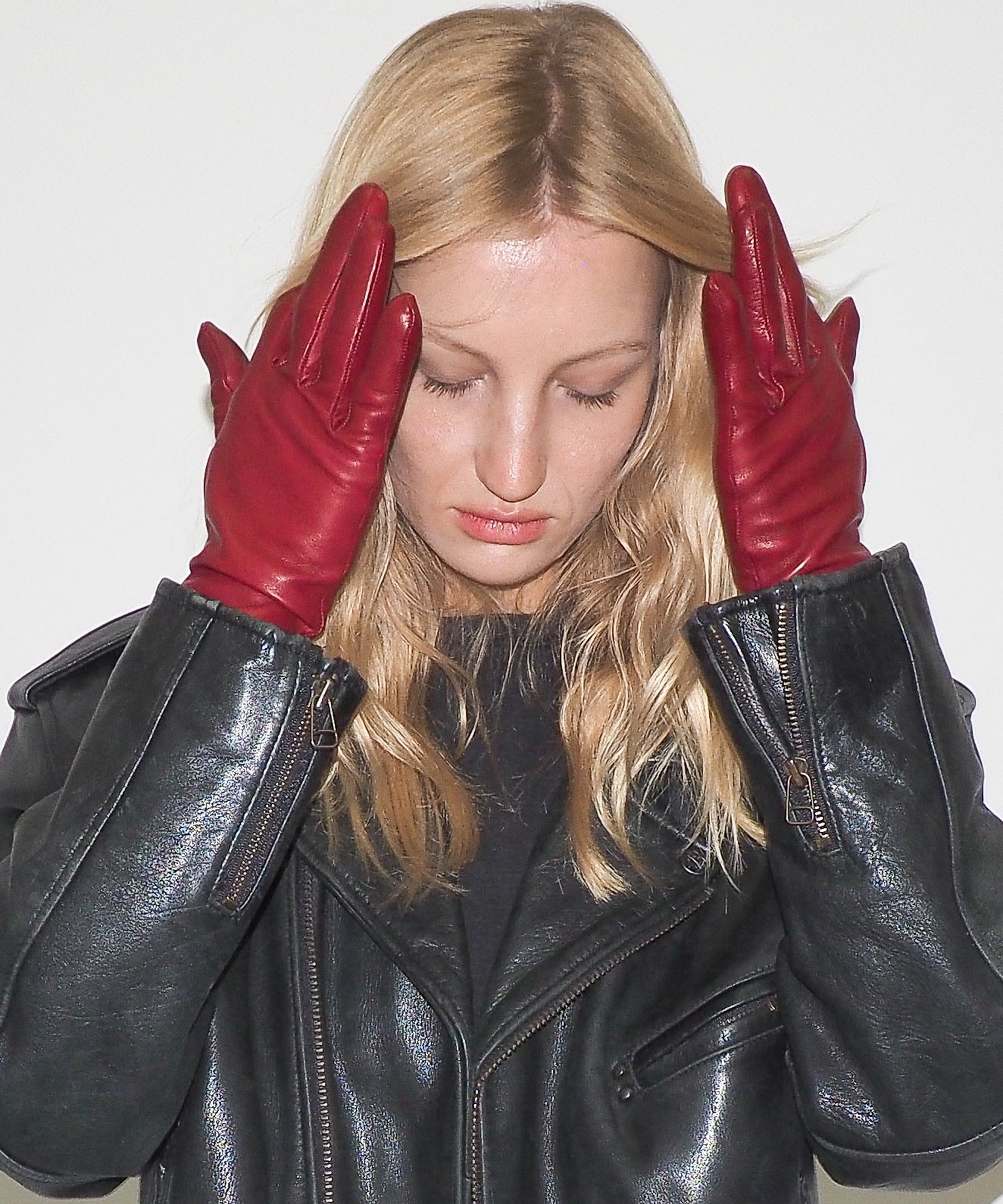 Woman wearing a black leather jacket and red gloves against a white background