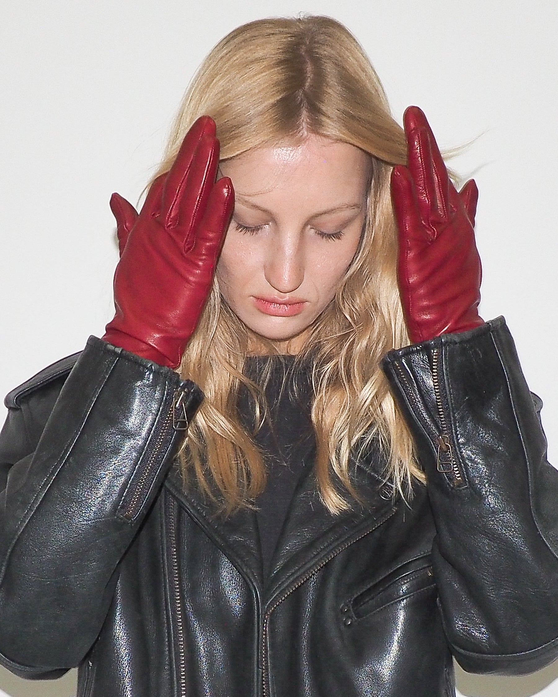 Woman wearing a black leather jacket and red gloves against a white background
