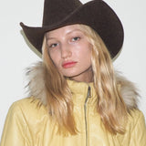 Person wearing a brown cowboy hat and yellow coat with fur hood against a white background