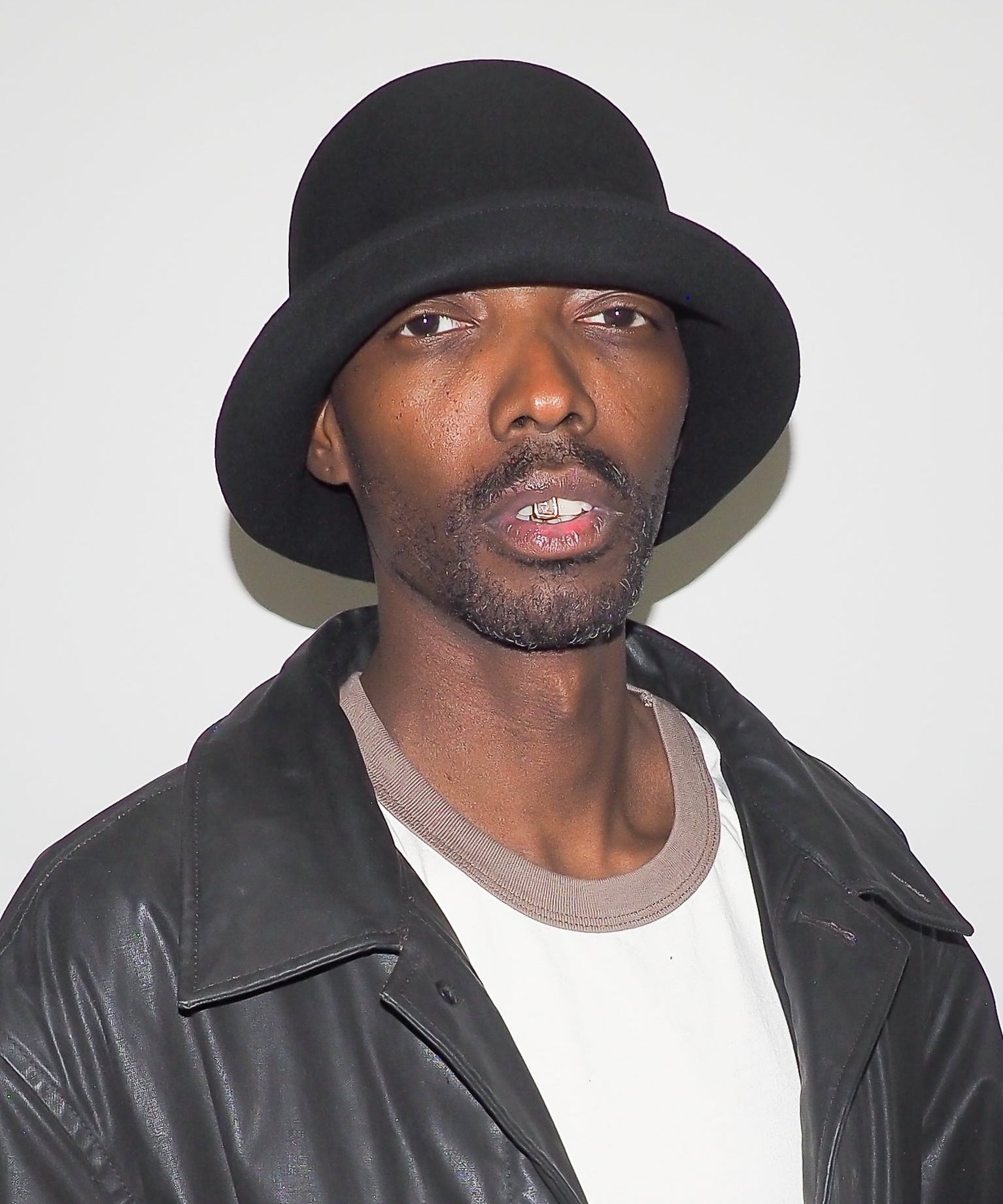 Man wearing a black hat and leather jacket against a white background