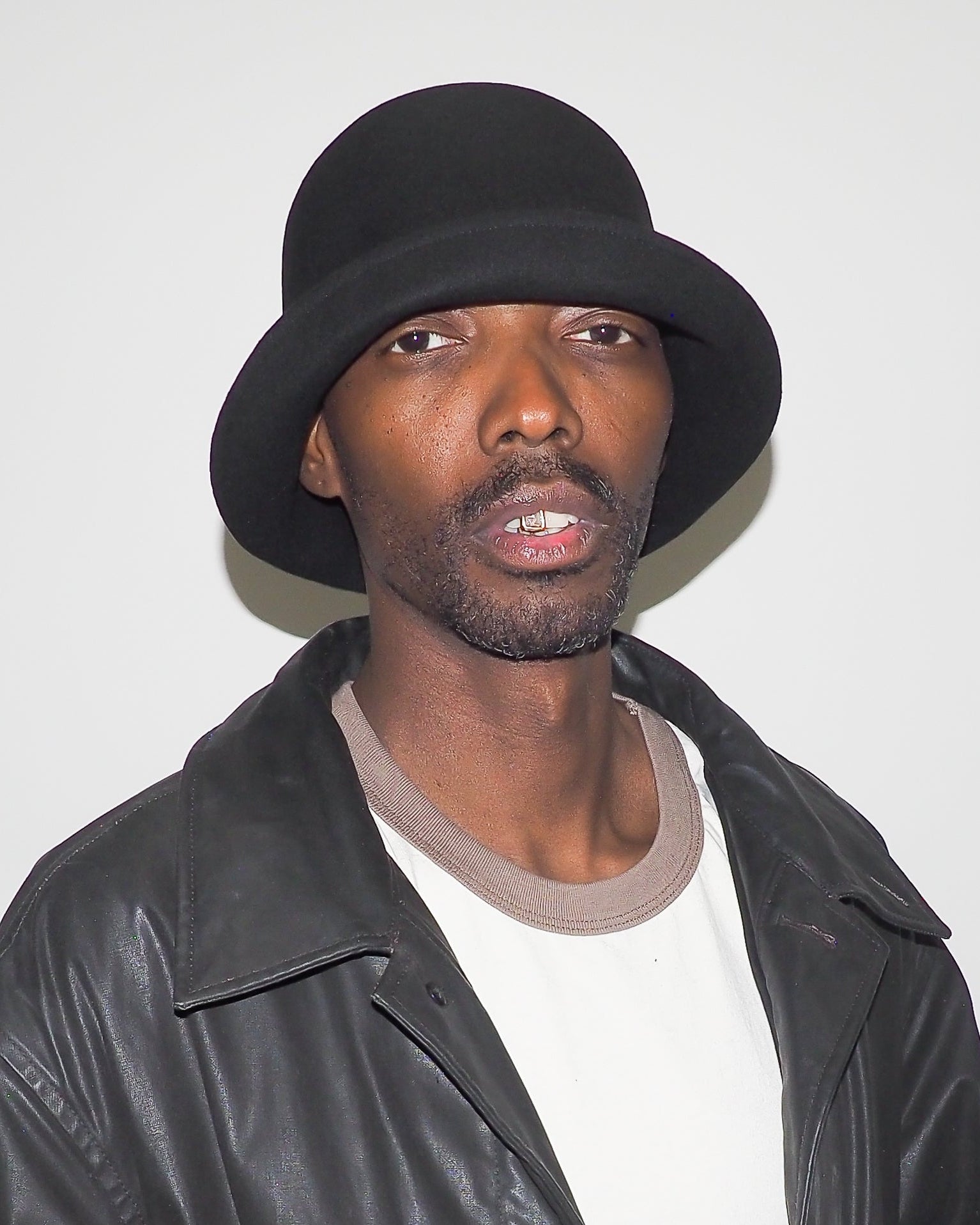 Man wearing a black hat and leather jacket against a white background