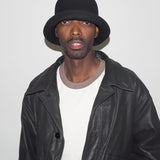 Person wearing a black leather jacket and hat against a plain background