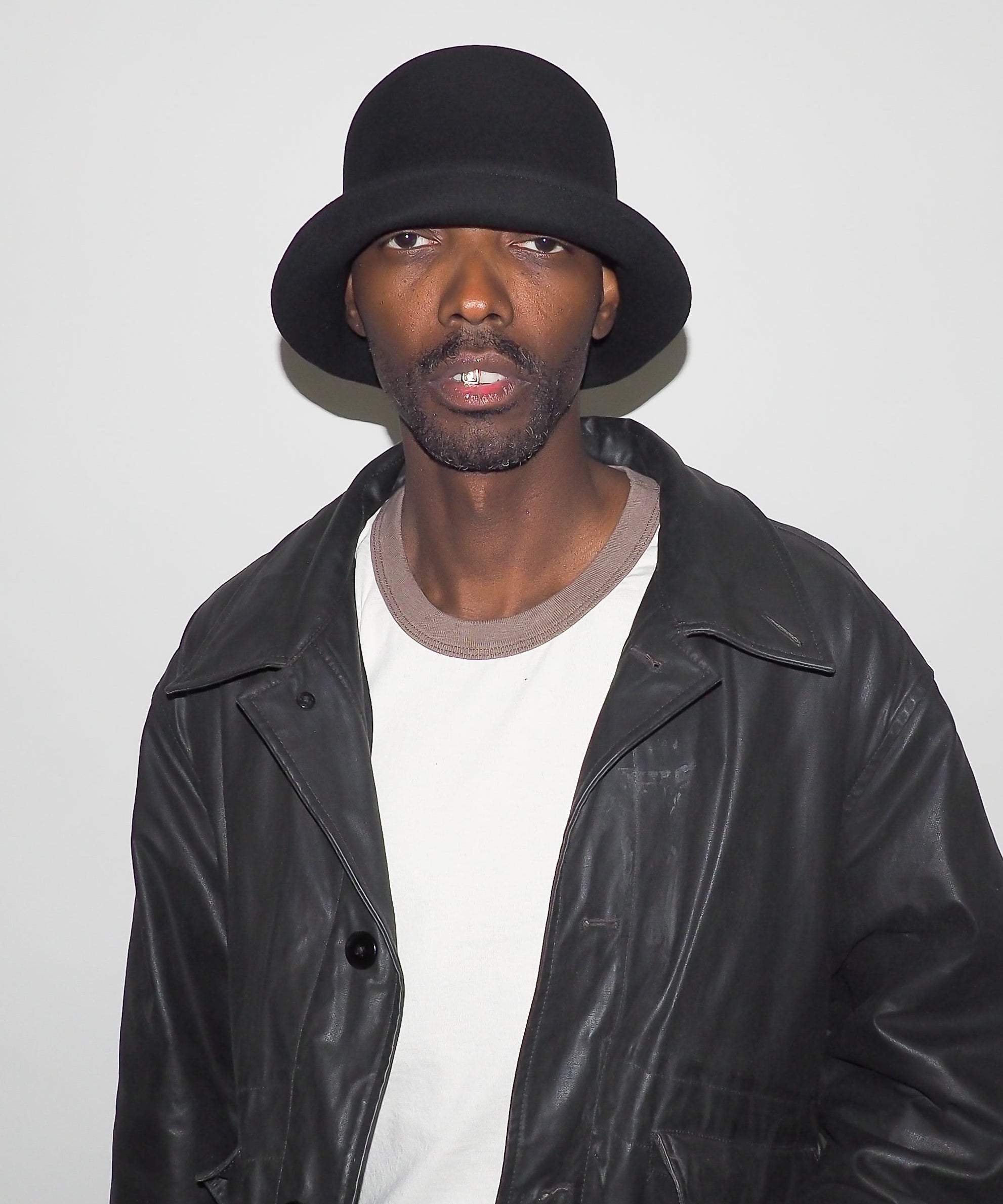 Person wearing a black leather jacket and hat against a plain background