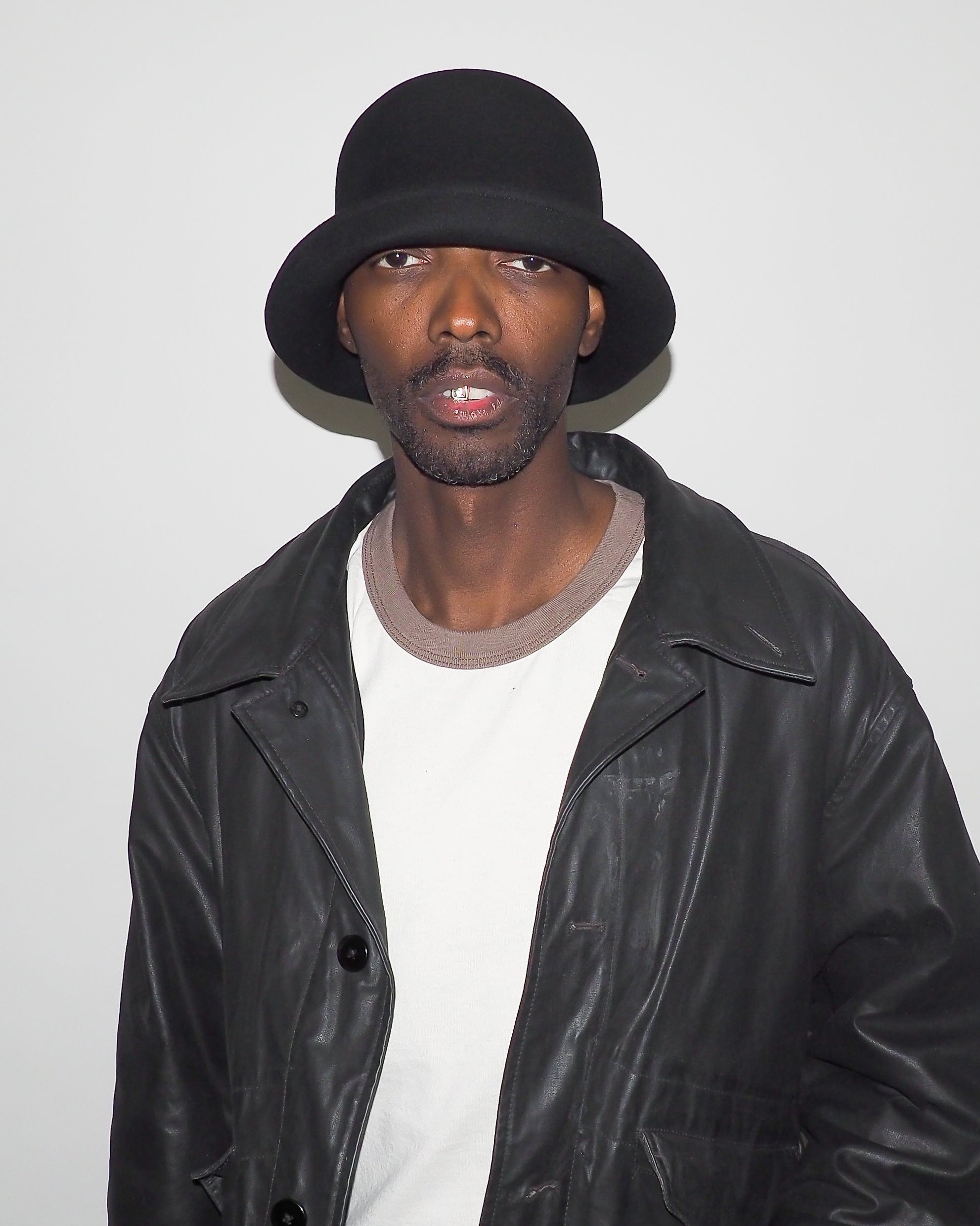 Person wearing a black leather jacket and hat against a plain background