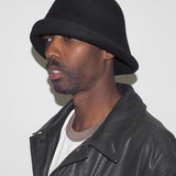 Man wearing a black bucket hat and leather jacket against a white background