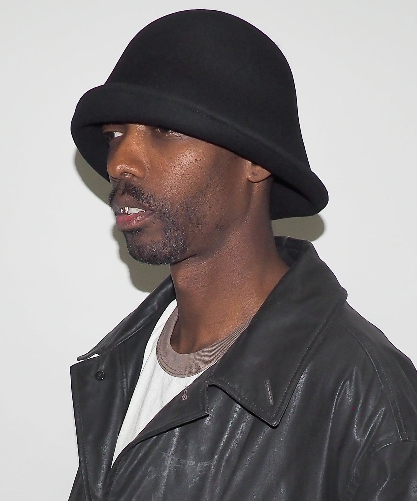 Man wearing a black bucket hat and leather jacket against a white background