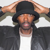 Person wearing a black hat and leather jacket against a white background