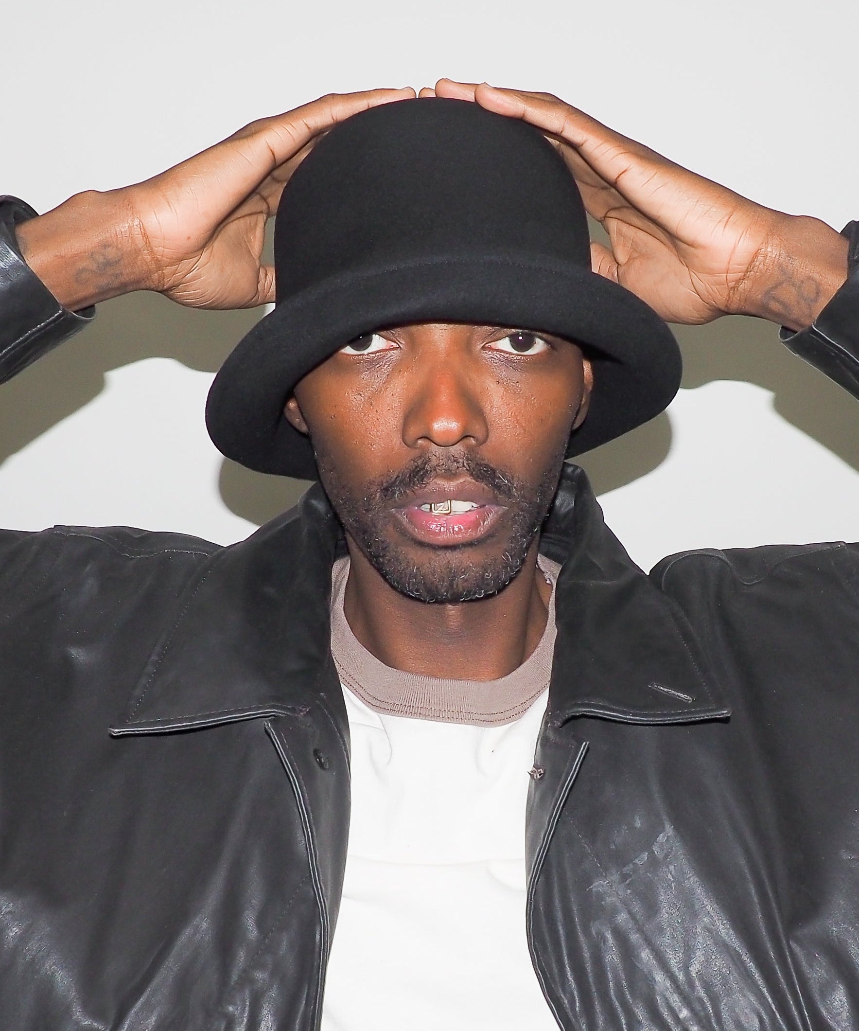 Person wearing a black hat and leather jacket against a white background