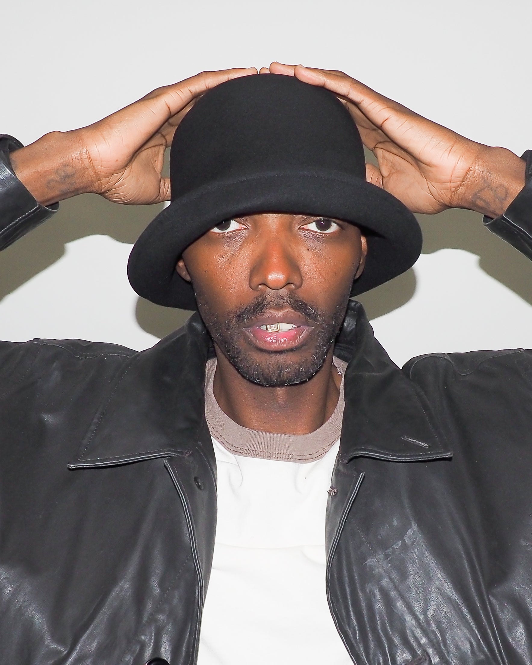 Person wearing a black hat and leather jacket against a white background