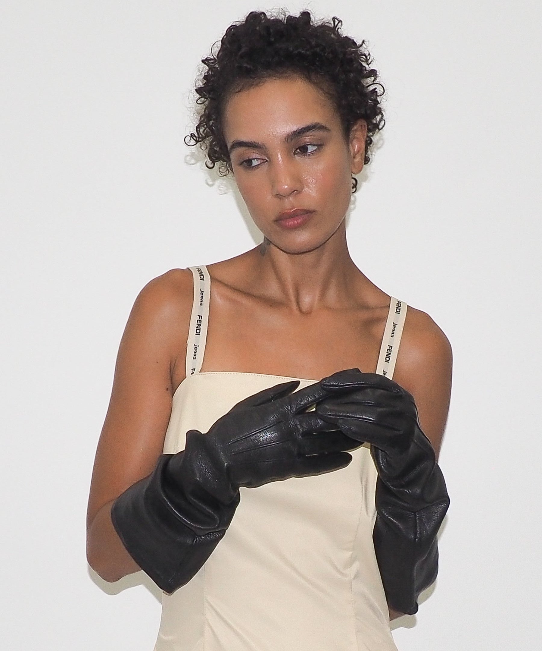 Woman wearing black gloves and a beige dress against a white background