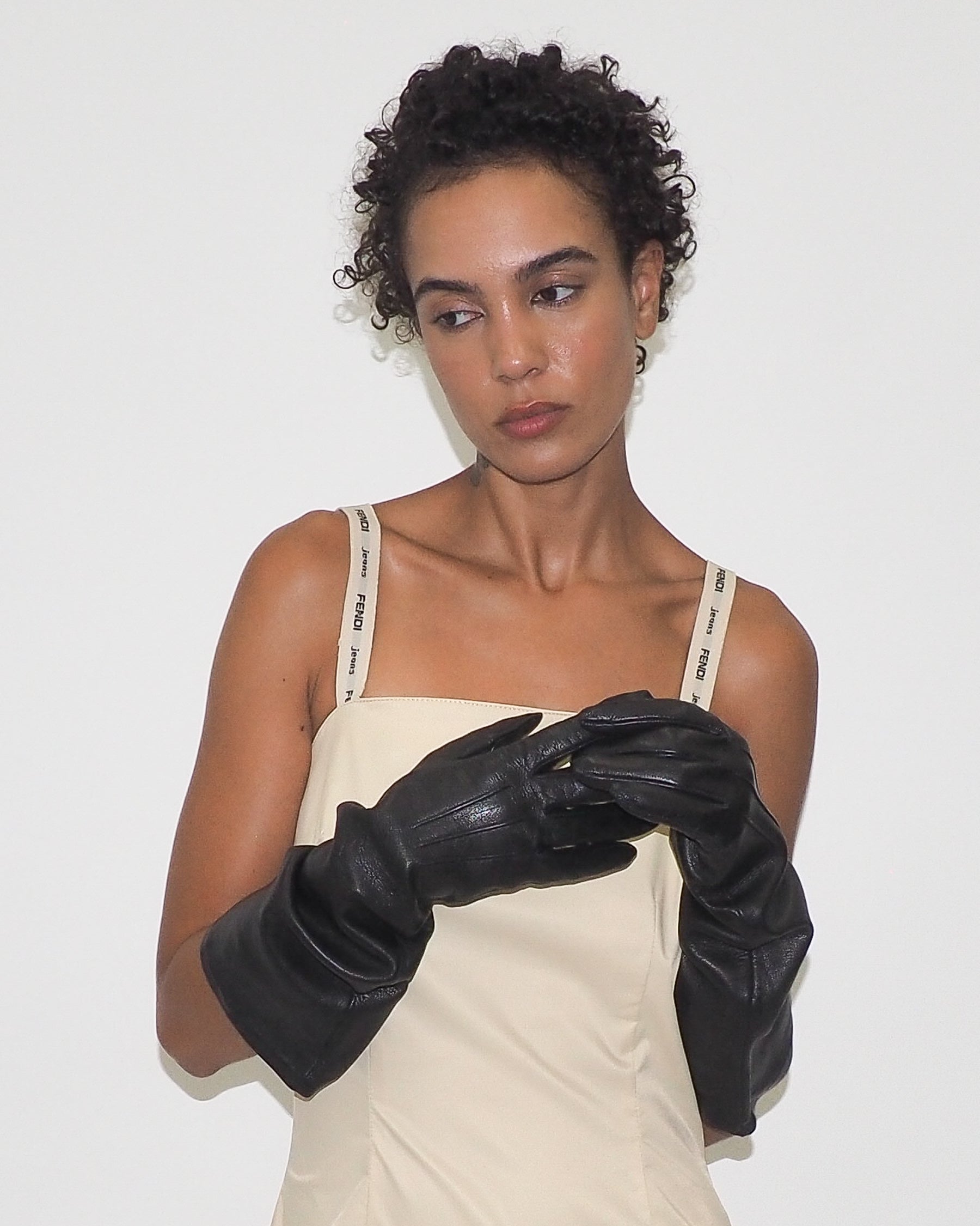 Woman wearing black gloves and a beige dress against a white background