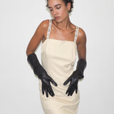 Woman wearing a beige dress and black gloves against a white background