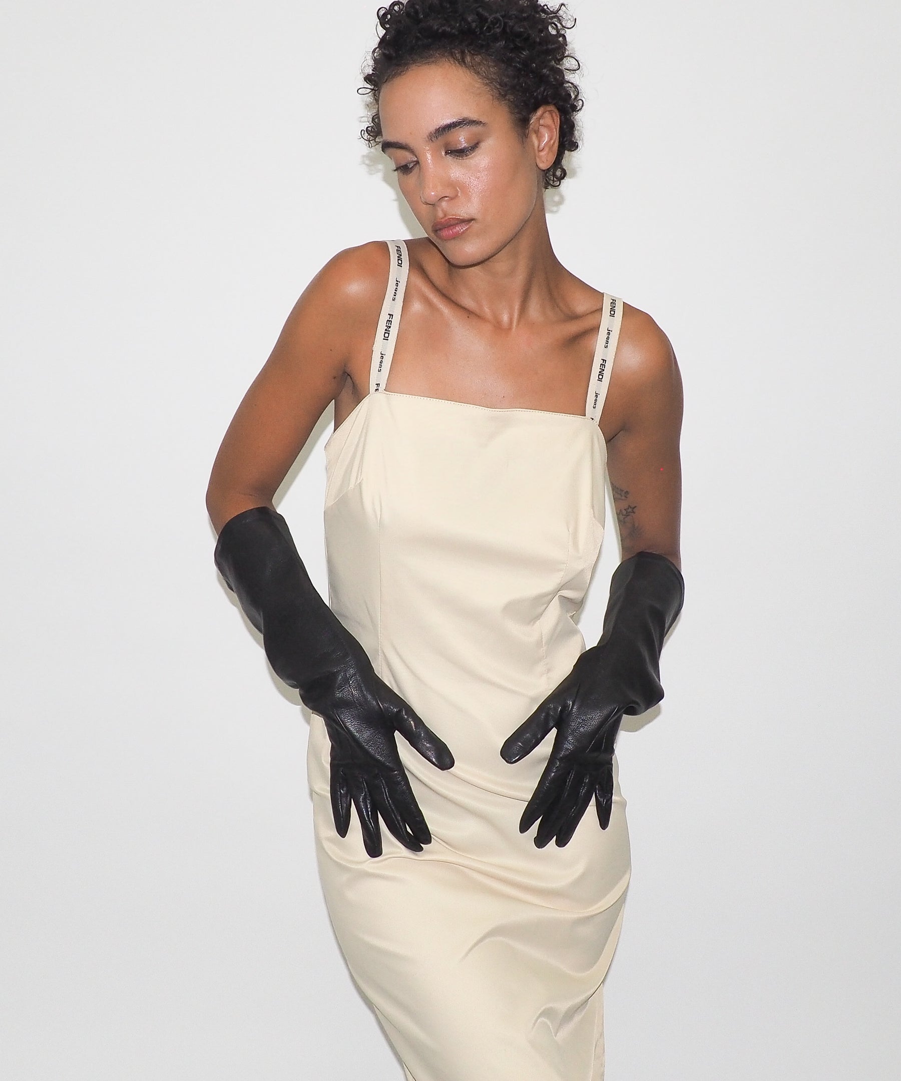 Woman wearing a beige dress and black gloves against a white background