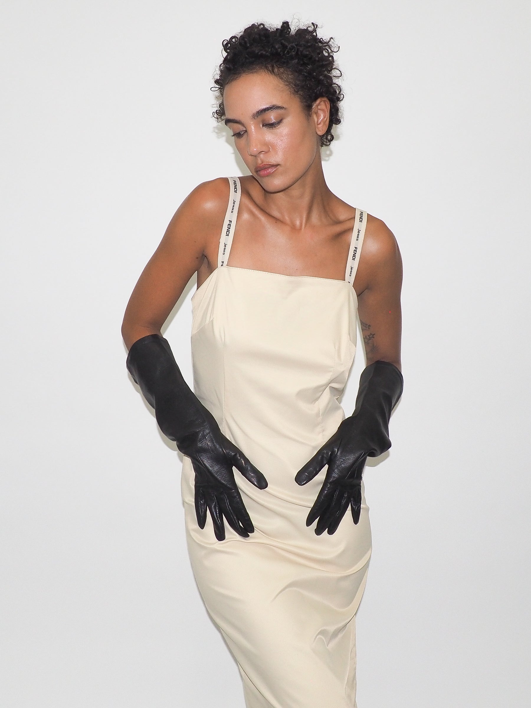 Woman wearing a beige dress and black gloves against a white background
