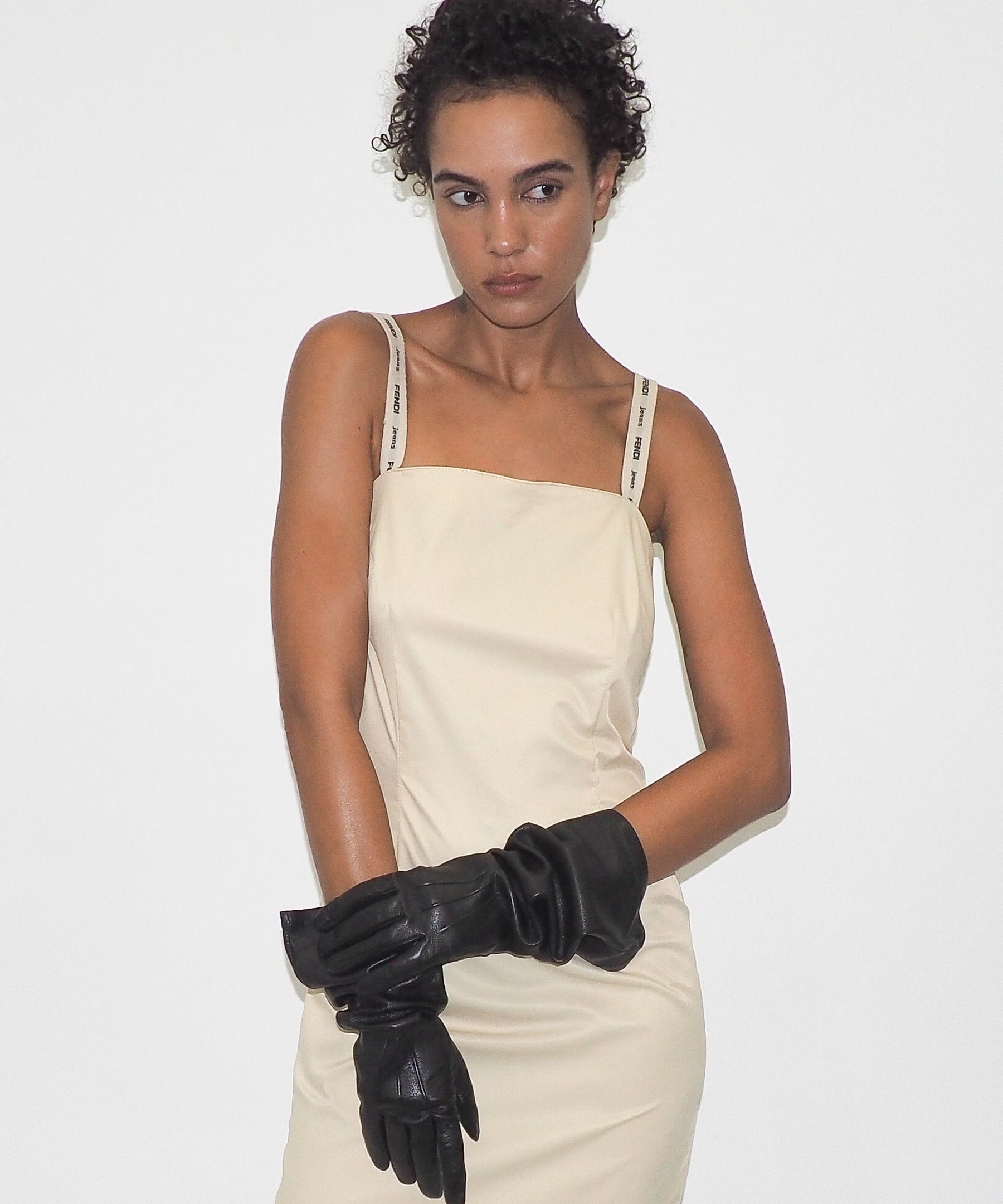 Woman wearing a beige dress and black gloves on a white background