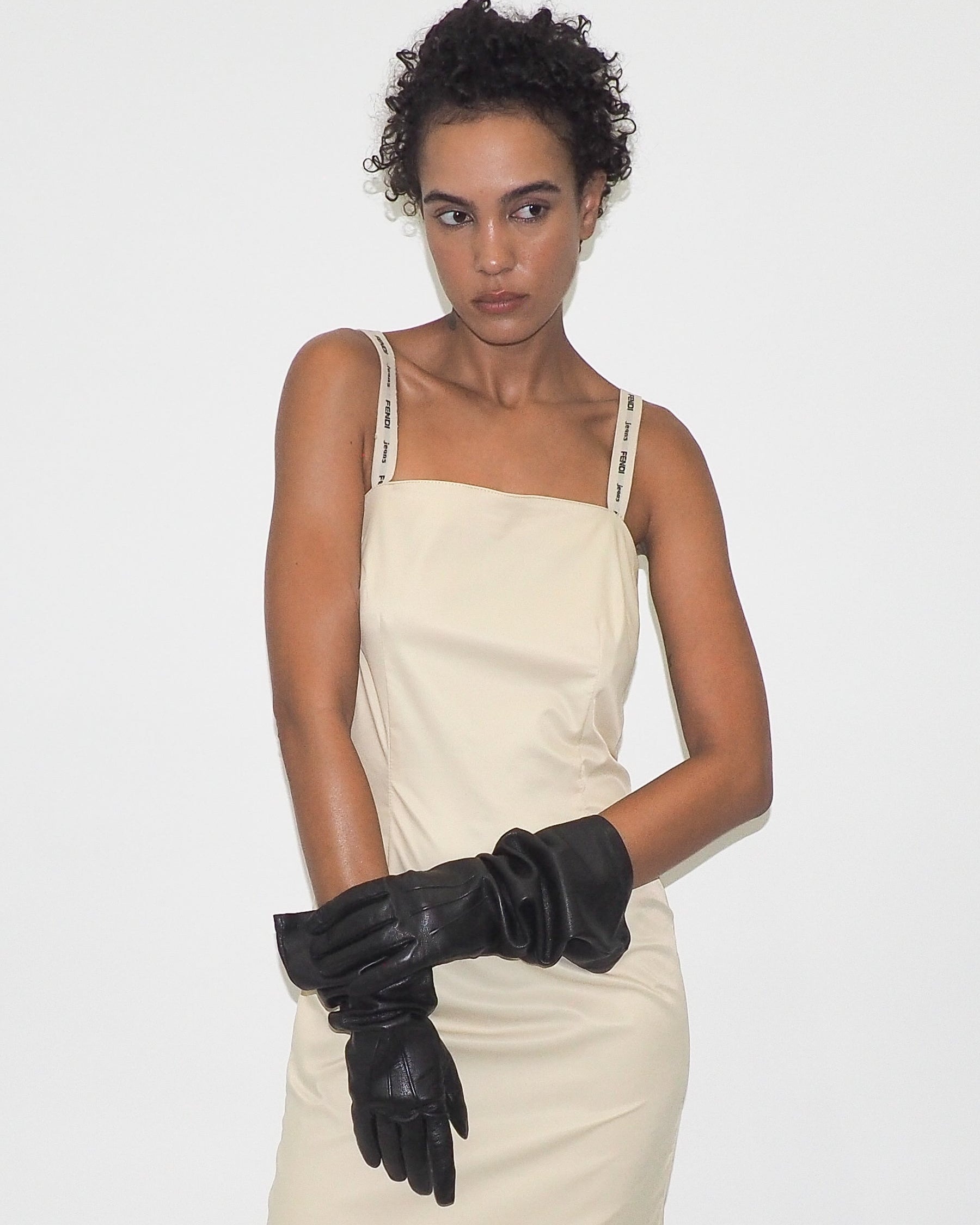 Woman wearing a beige dress and black gloves on a white background