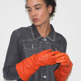 Person wearing a black denim jacket and orange leather gloves against a white background