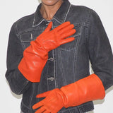 Person wearing a denim jacket and bright orange gloves against a plain background