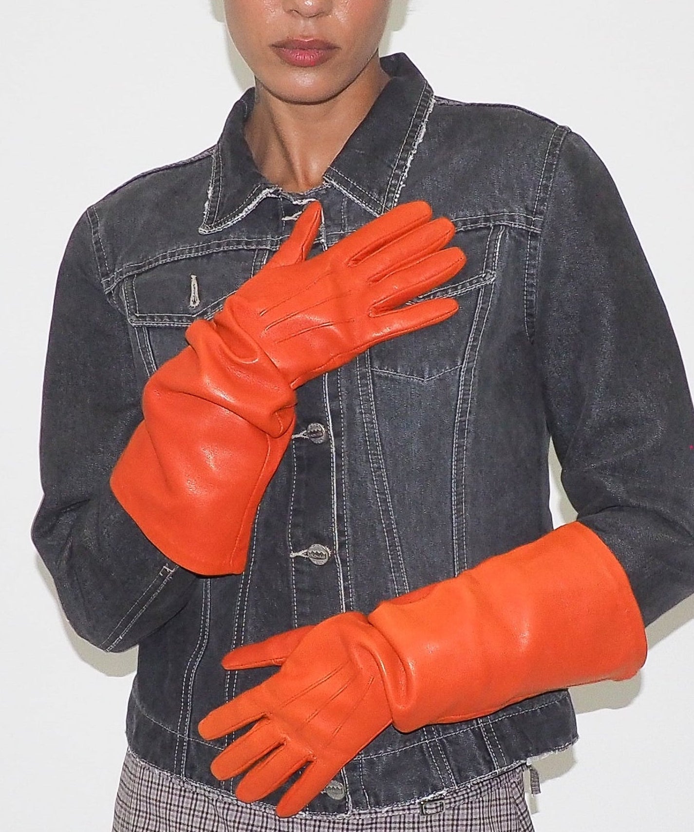 Person wearing a denim jacket and bright orange gloves against a plain background