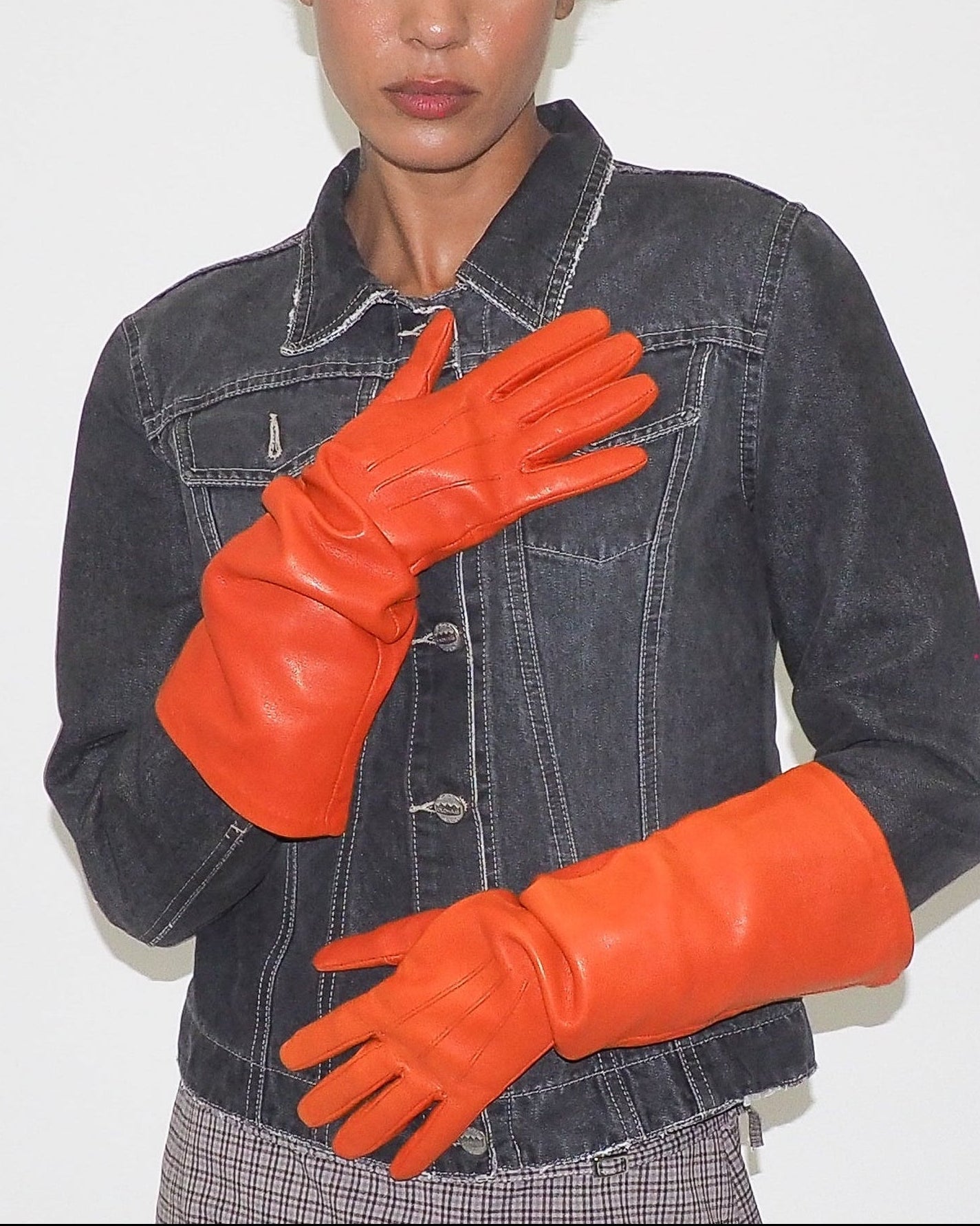 Person wearing a denim jacket and bright orange gloves against a plain background