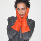Person wearing orange gloves and a denim jacket on a plain background