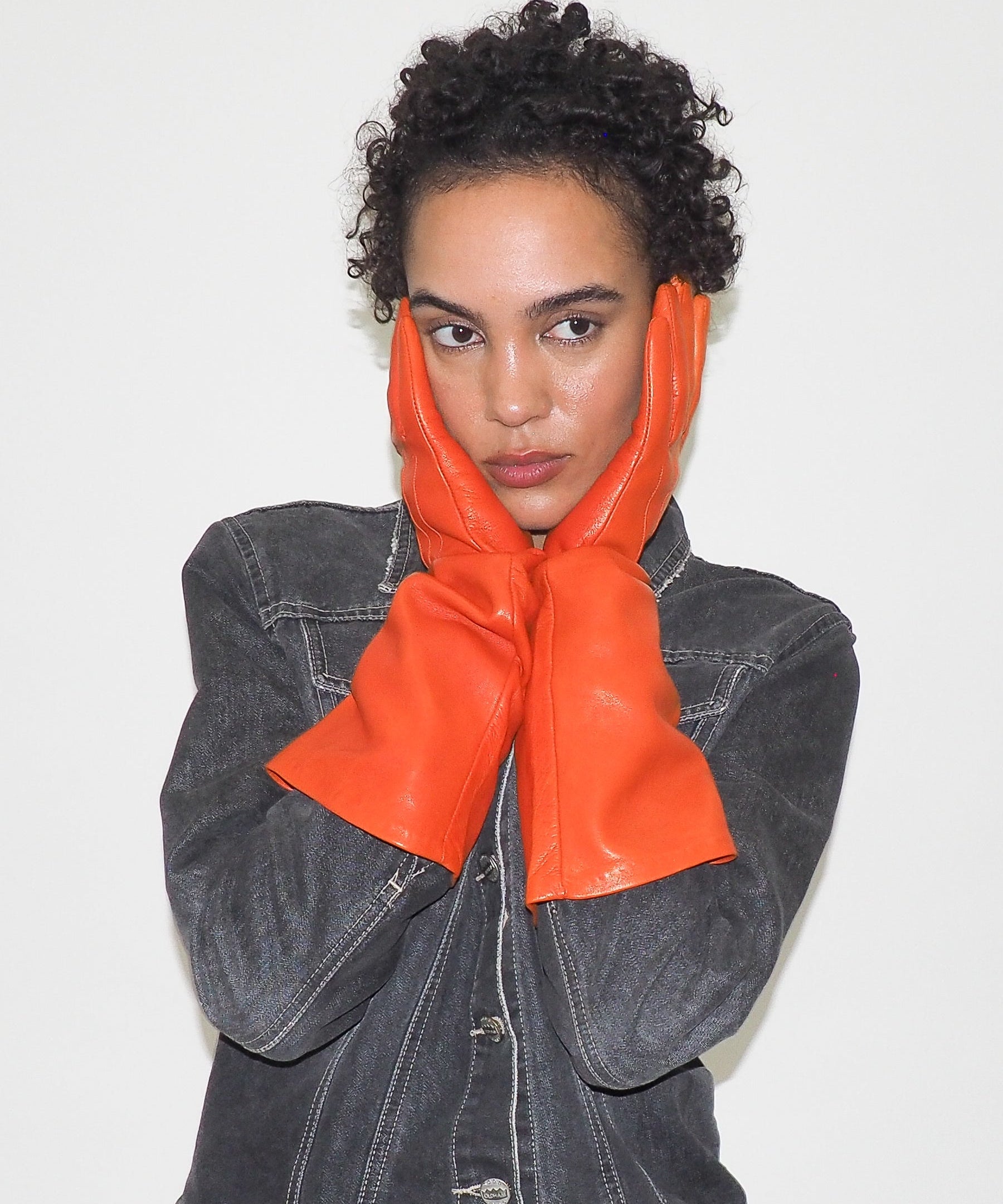 Person wearing orange gloves and a denim jacket on a plain background