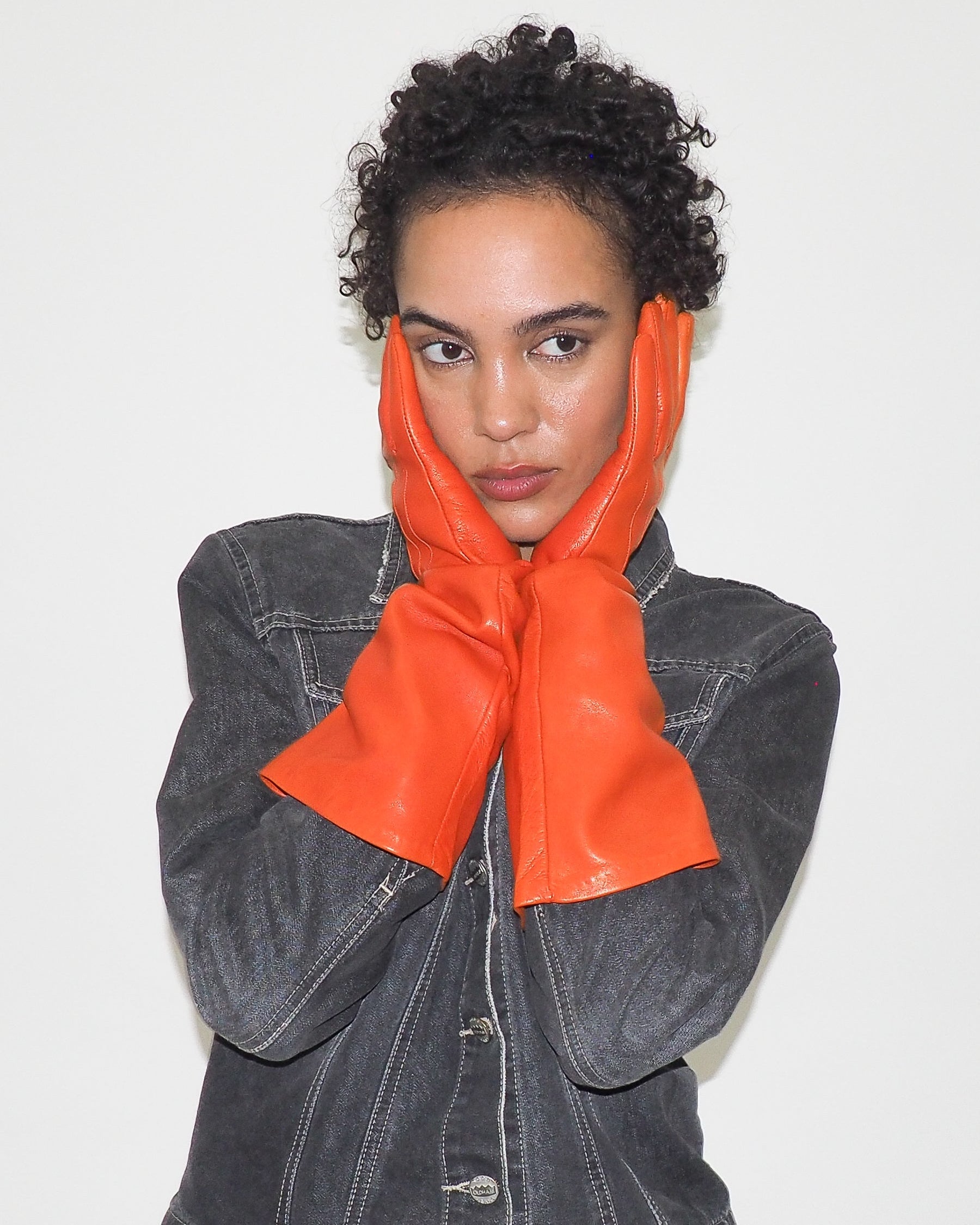 Person wearing orange gloves and a denim jacket on a plain background
