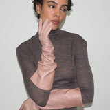 Woman wearing a brown turtleneck sweater and beige gloves against a plain background