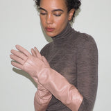 Woman wearing a brown turtleneck sweater and pink gloves against a white background