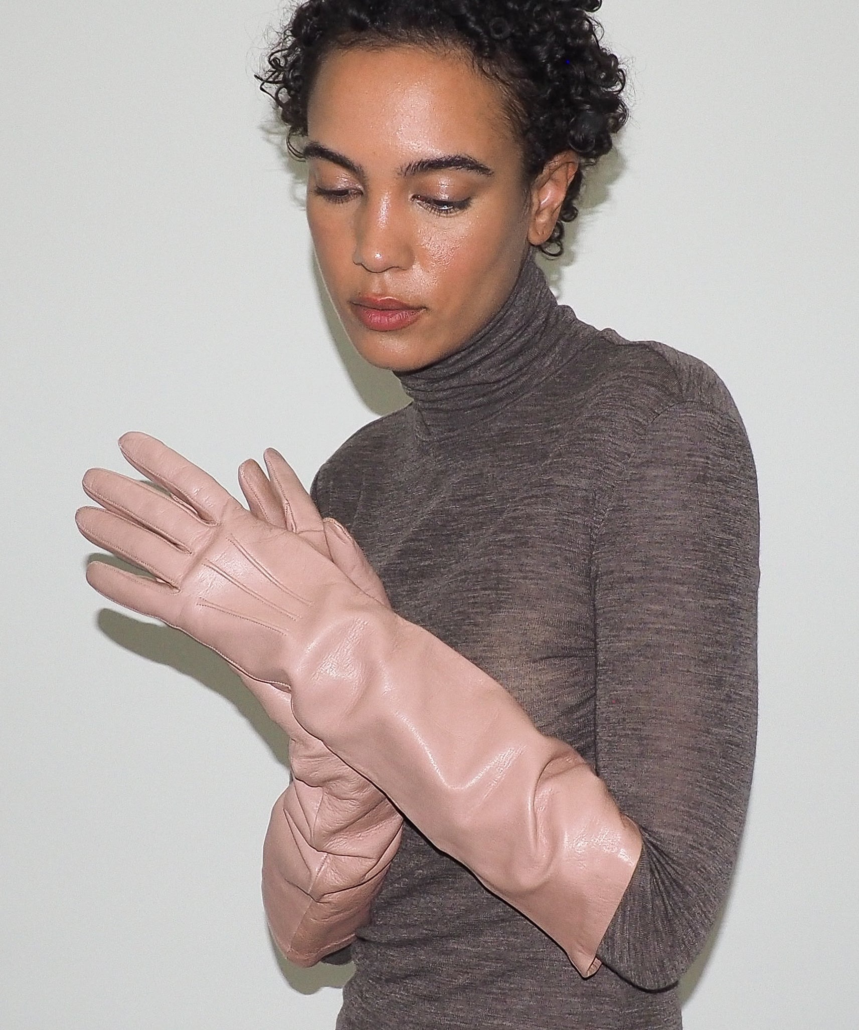 Woman wearing a brown turtleneck sweater and pink gloves against a white background