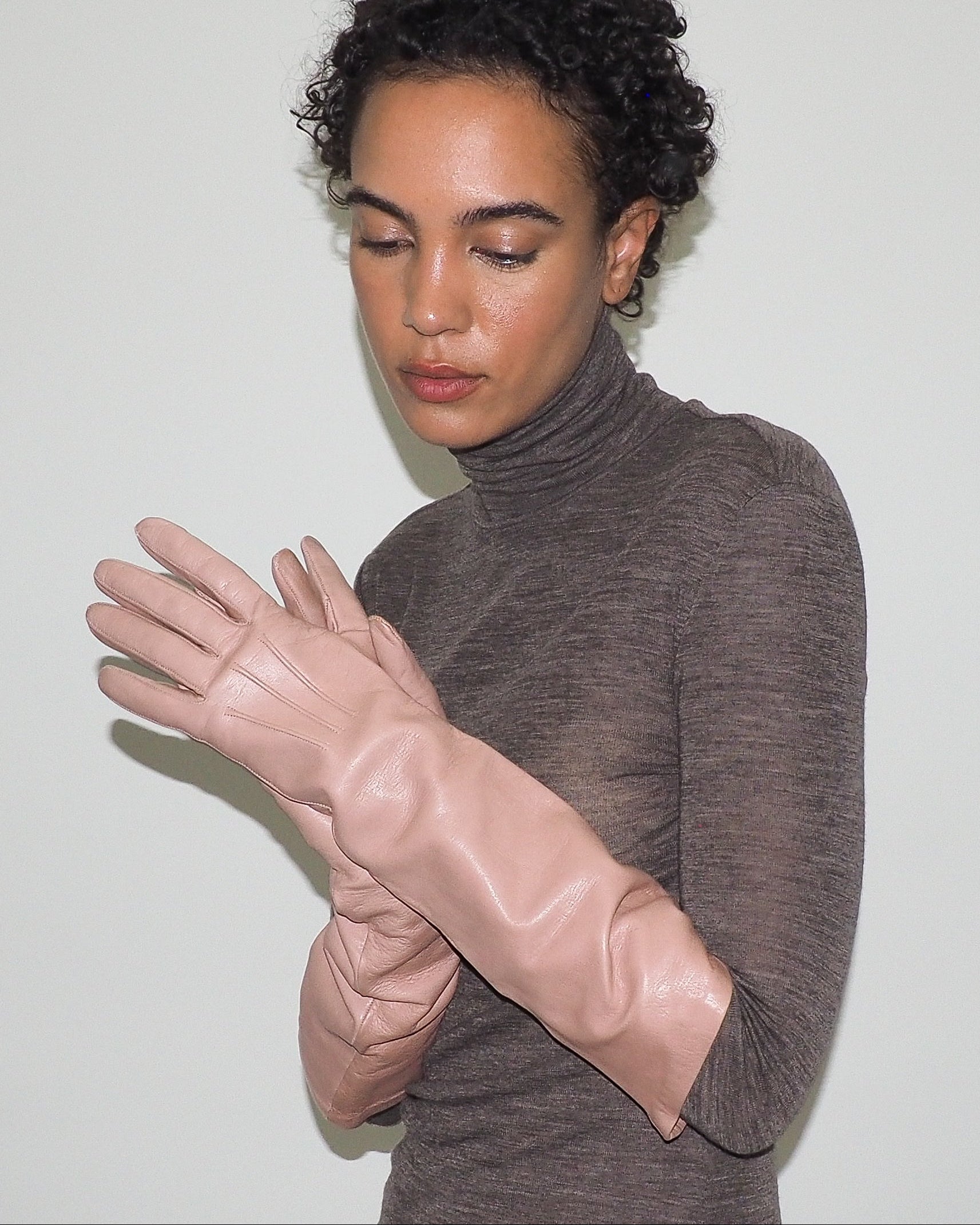 Woman wearing a brown turtleneck sweater and pink gloves against a white background