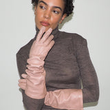 Woman wearing a brown turtleneck sweater and beige gloves against a white background