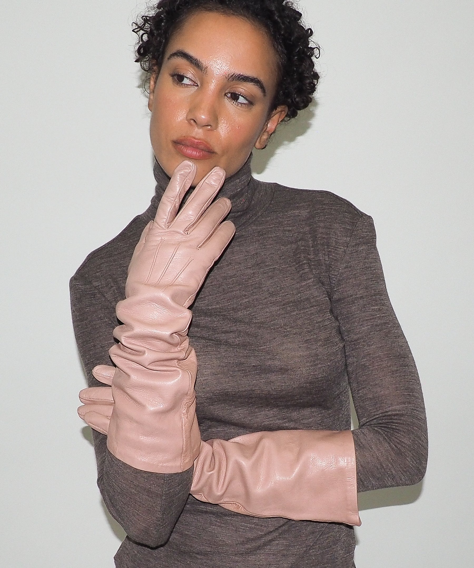 Woman wearing a brown turtleneck sweater and beige gloves against a white background